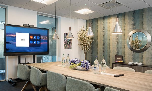 Elegant und hell möbilierter Konferenzraum mit großem isch und Avocor Display mit dem Zoom Rooms Startbildschirm
