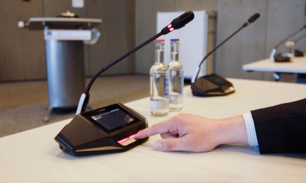 Eine Hand die eine digitale Sprechstelle in einem Sitzungssaal bedient