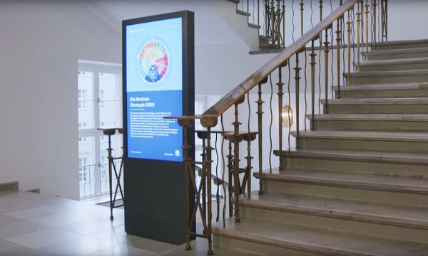 Ein Display mit Digital Signage neben einem Treppenaufgang