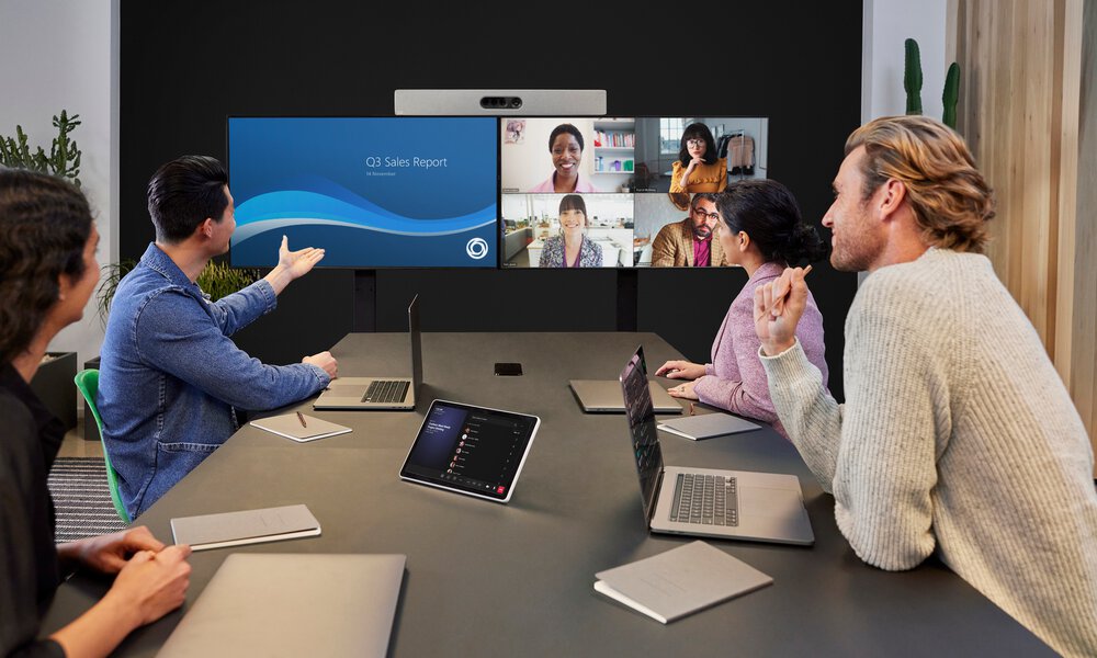Vier Personen in einem Konferenzraum mit Cisco Ausstattung in einer Microsoft Teams Videokonferenz an einem Doppelbildschirm