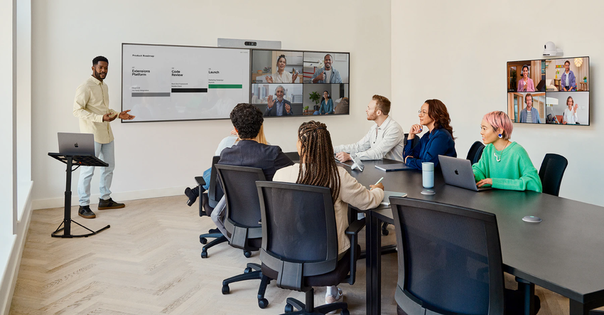 Eine gruppe sitzt an einem Konferenztisch und hört einem Mann zu, der vor an einem Display steht und eine Präsentation hält, es wird das Cisco Room Kit EQ verwendet