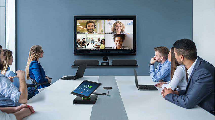 Eine Gruppe sitzt an einem Konferenztisch und guckt zu einem Display an der Wand, wo vier weitere Remote Teilnehmer zu sehen sind, verwendet wird das Lenovo ThinkSmart Hub 500